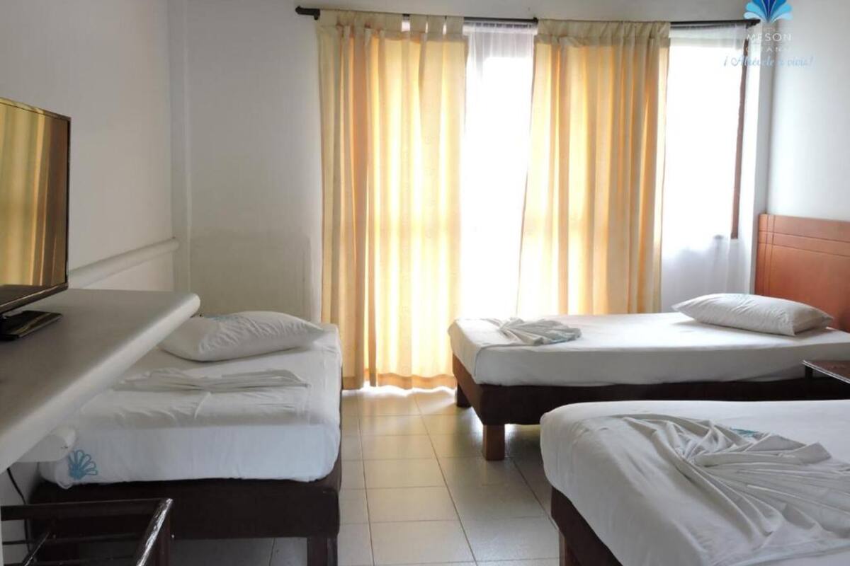 A hotel room with two beds, a TV, and a window with curtains.