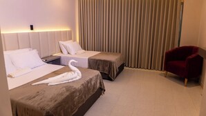 Habitación de hotel con dos camas, una silla roja y un ventanal con cortinas.