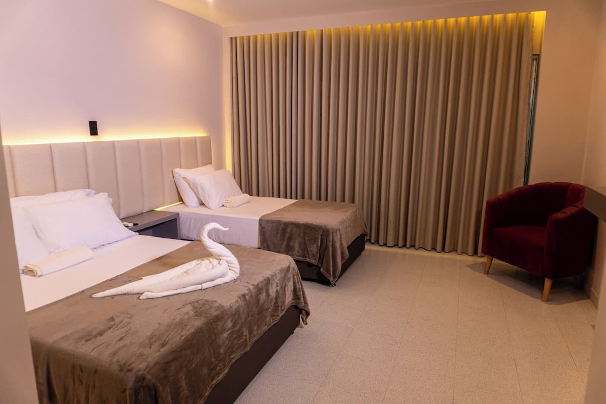 A hotel room with two beds, a red chair, and a large window with curtains.