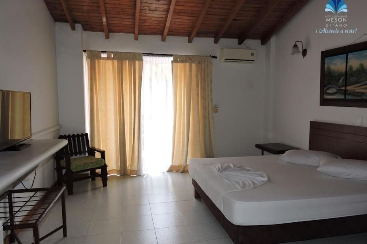 Una habitación de hotel con cama, escritorio, silla y ventana con cortinas.