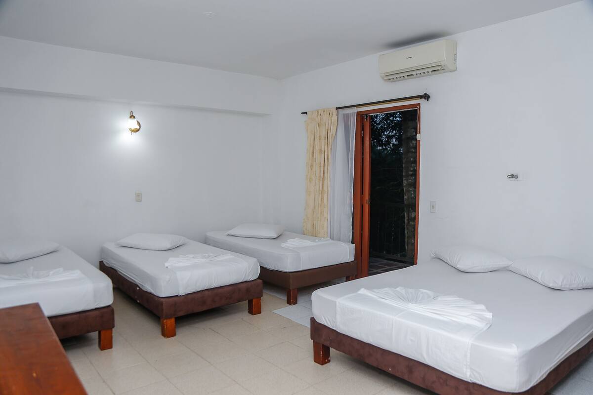 A room with four single beds, a wooden bench, a wall-mounted air conditioner, and a sliding glass door.