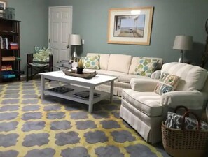 Cozy living space with a sofa, armchair, coffee table, bookshelf, and framed picture.