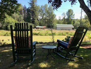 Relax in a serene outdoor setting with two comfortable rocking chairs and a small table amidst a lush green landscape.