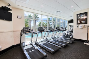 A gym with treadmills aligned in a row, large windows, and a pool view.