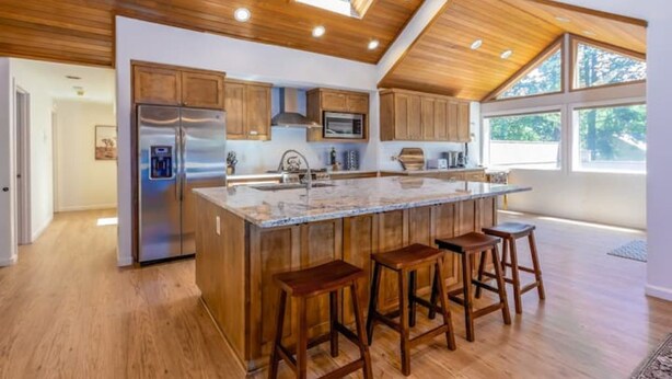 A modern kitchen with wooden cabinets, a stainless steel refrigerator, a microwave, and a large island with stools. - 10 SHARC/basketball ct/ac/private hot tub+bikes +snow sleds (Sunriver)