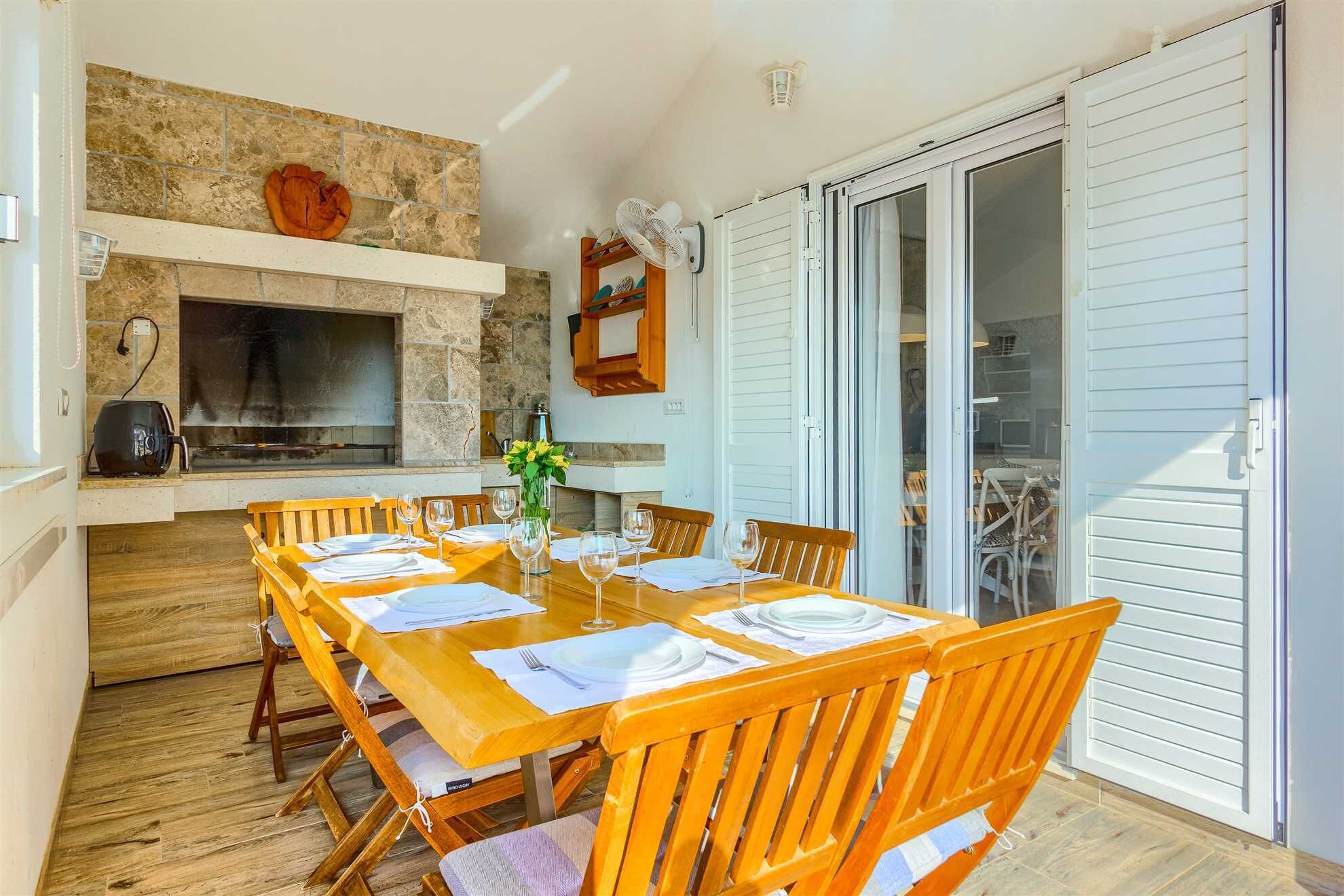 Un espace extérieur aménagé pour les repas, avec une cheminée en pierre, des chaises en bois et une table dressée pour quatre personnes.