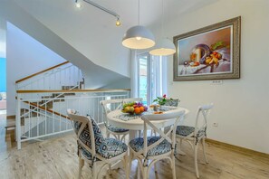 A dining area with a white table, patterned chairs, and a fruit bowl. A staircase is visible in the background. - Villa Belleza - sea views, heated pool, 70m to the beach by MyWaycation (Rogoznica)