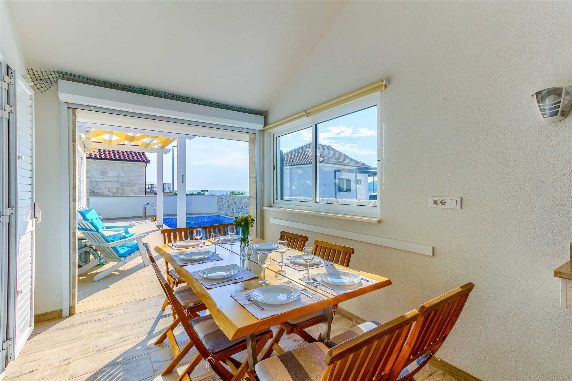 Un espace repas avec une table dressée pour quatre personnes, une piscine et une vue sur la mer.
