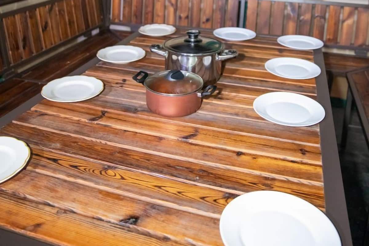 Un comedor con una mesa de madera dispuesta para seis personas, una olla de cobre y una jarra de vidrio.
