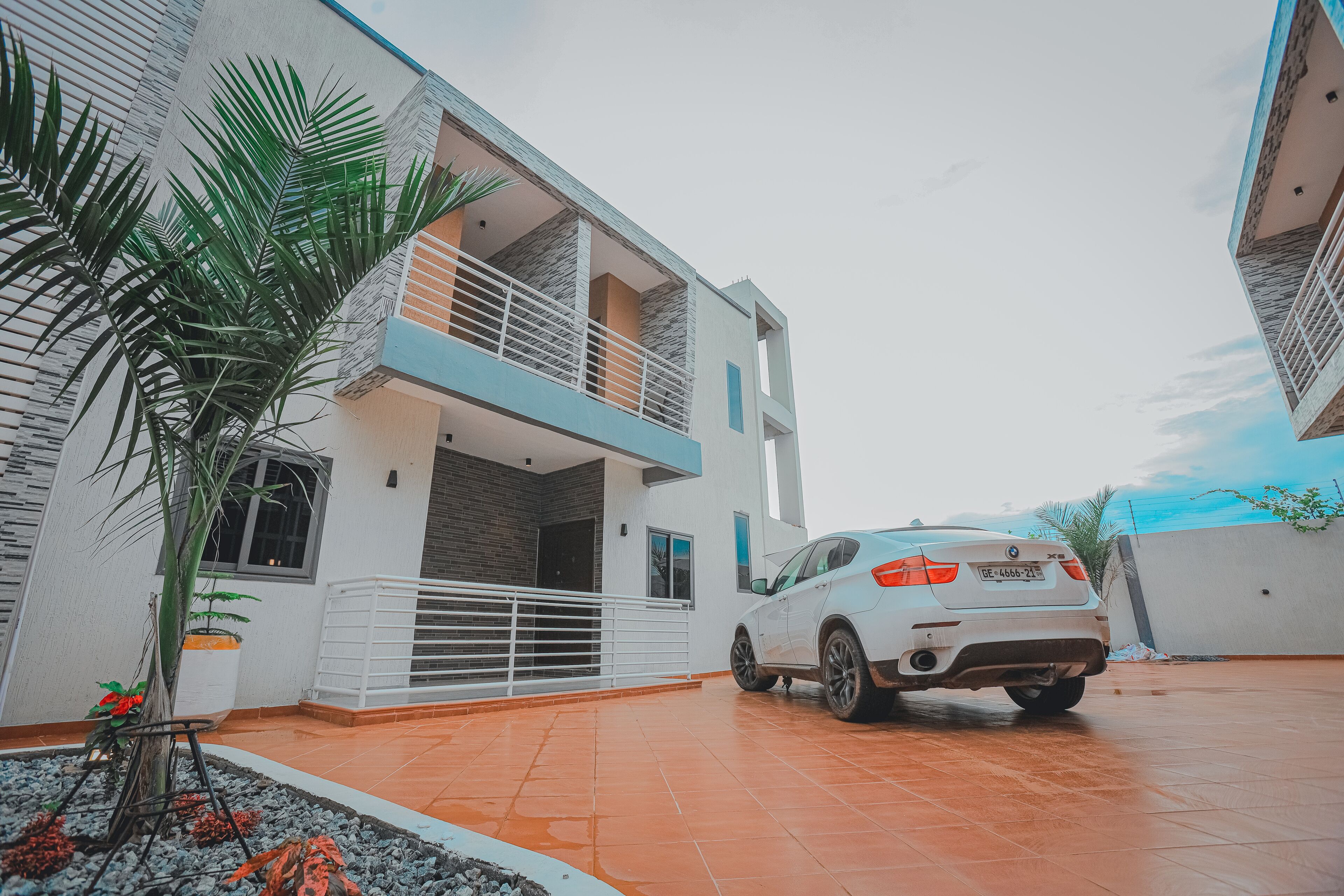 A modern two-story house with a white exterior, a balcony, and a parked white car.