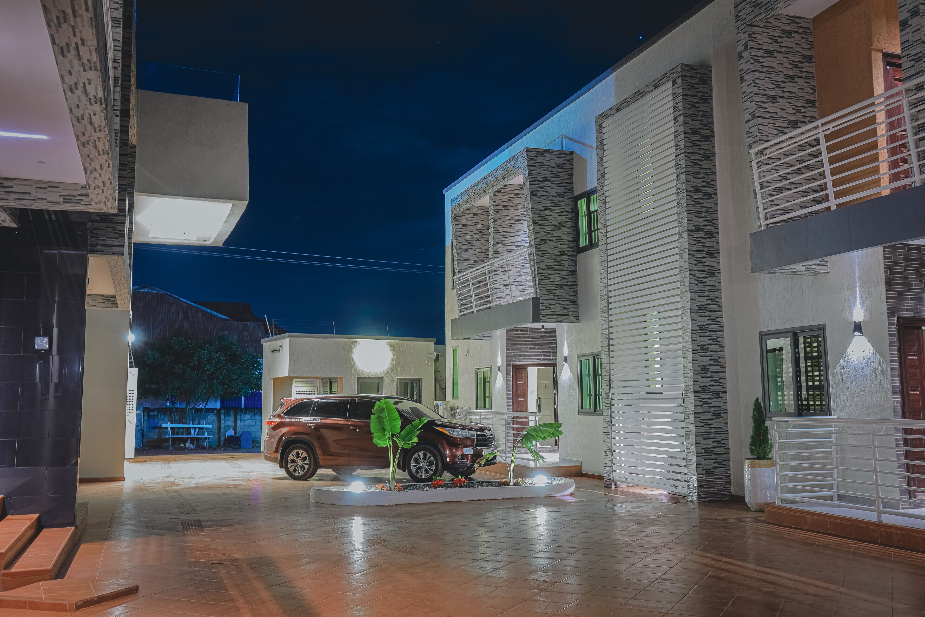 Un edifici residencial modern amb un pati espaiós, un cotxe estacionat al centre i una entrada ben il·luminada.