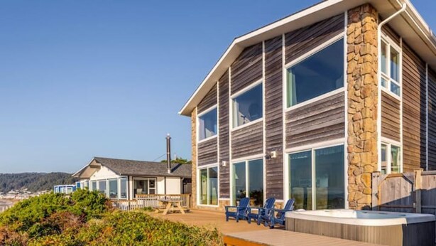 Ein zweistöckiges Haus mit großen Fenstern, einer Steinsäule und einer Terrasse mit Stühlen und einem Whirlpool.