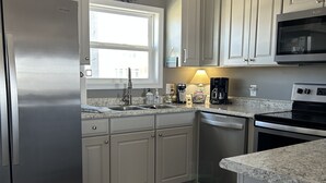 A modern kitchen with white cabinets, stainless steel appliances, and a decorative wall clock. - Sea La Vie (Ocean Isle Beach)