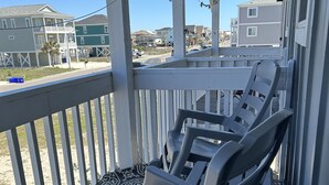 A covered outdoor area with a patterned floor, white railings, and two plastic chairs. - Sea La Vie (Ocean Isle Beach)