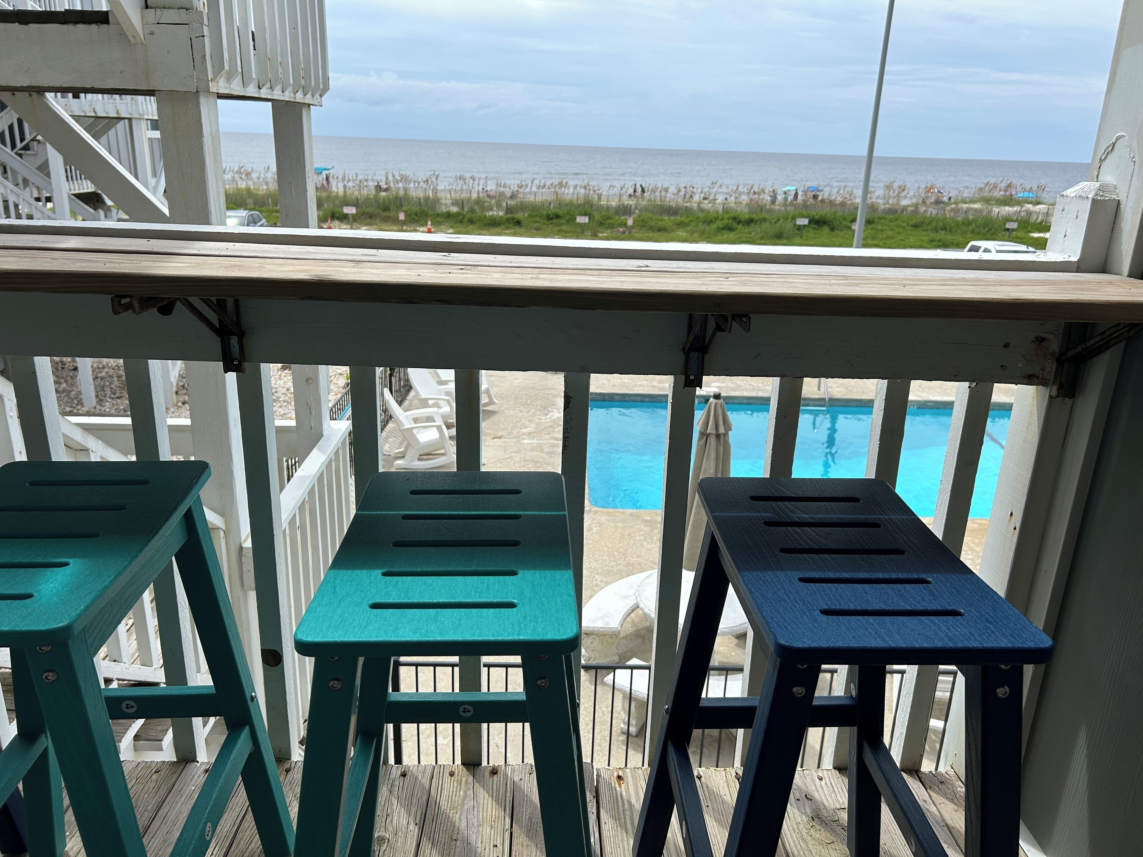A wooden deck with a pool and beach view.