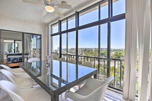 A modern dining area with a glass table and white chairs, large windows offering a city view. - < 1 Mi to Siesta Key Beach: Condo w/ Pool (Siesta Key)