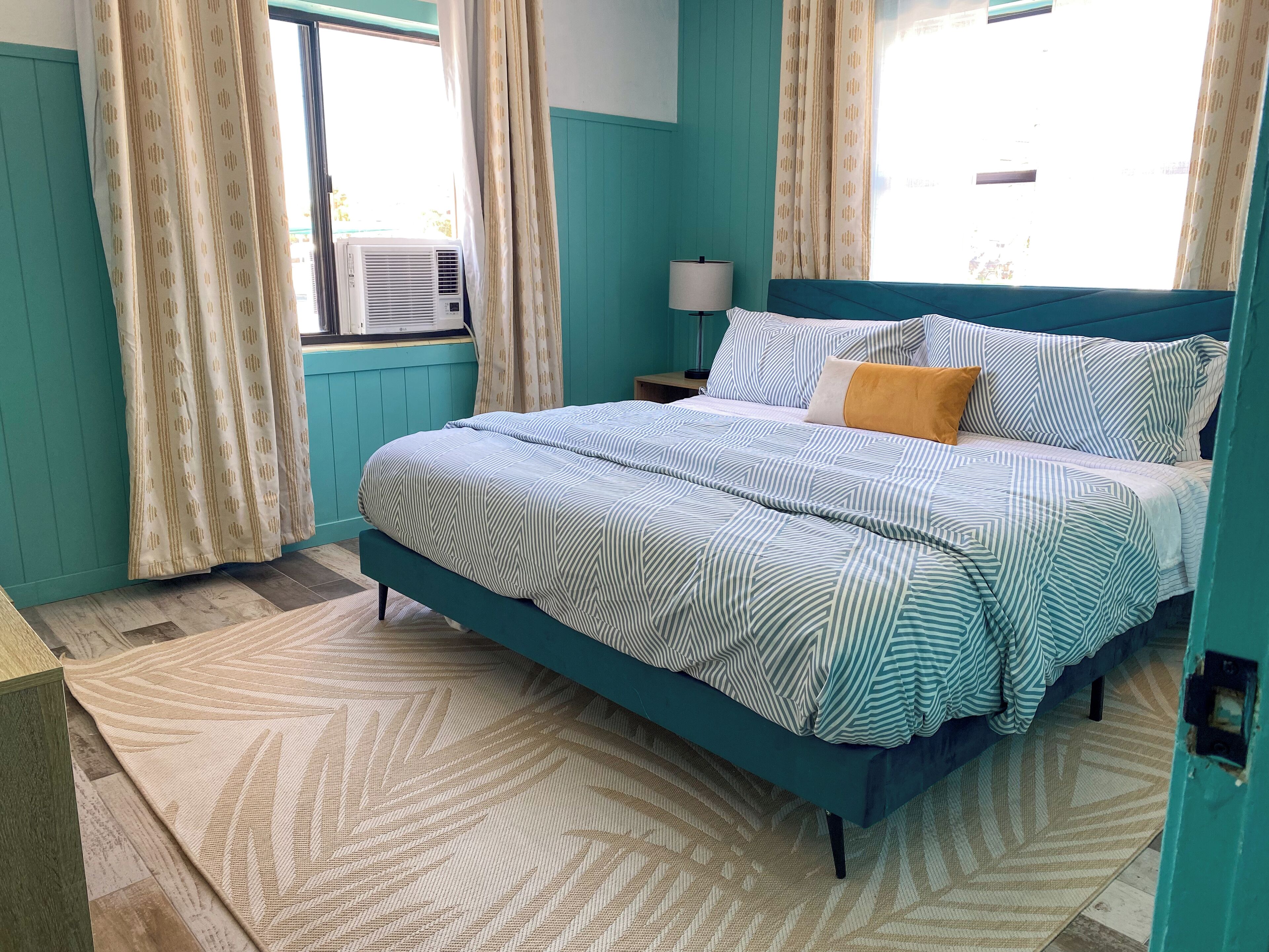 A bedroom with a bed, curtains, a lamp, and a window.
