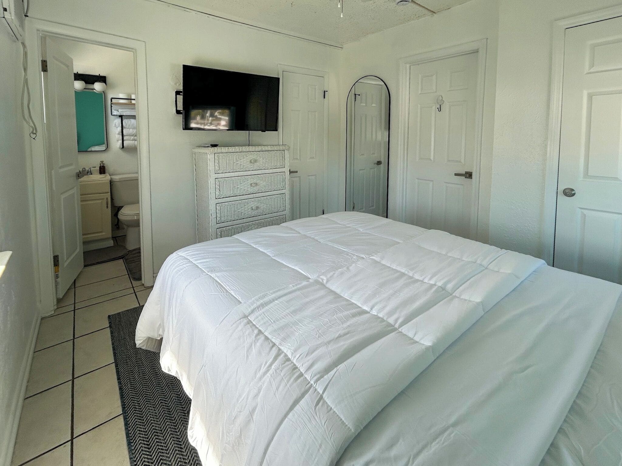 Ein Schlafzimmer mit einem großen Bett, einem an der Wand montierten Fernseher und einem durch eine offene Tür einsehbaren Badezimmer.