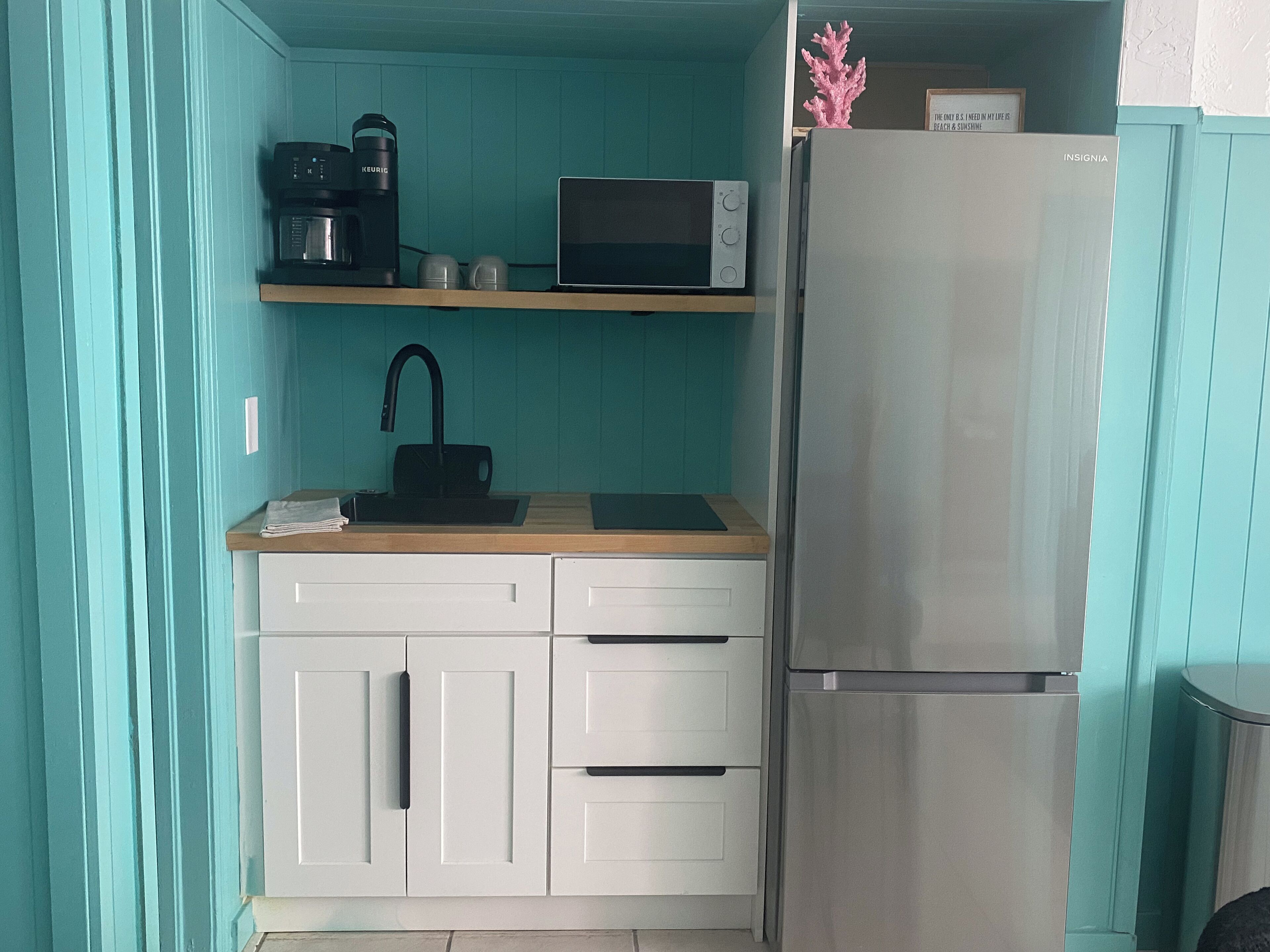 A compact kitchen with white cabinets, a stainless steel refrigerator, a microwave, a coffee maker, and a sink.