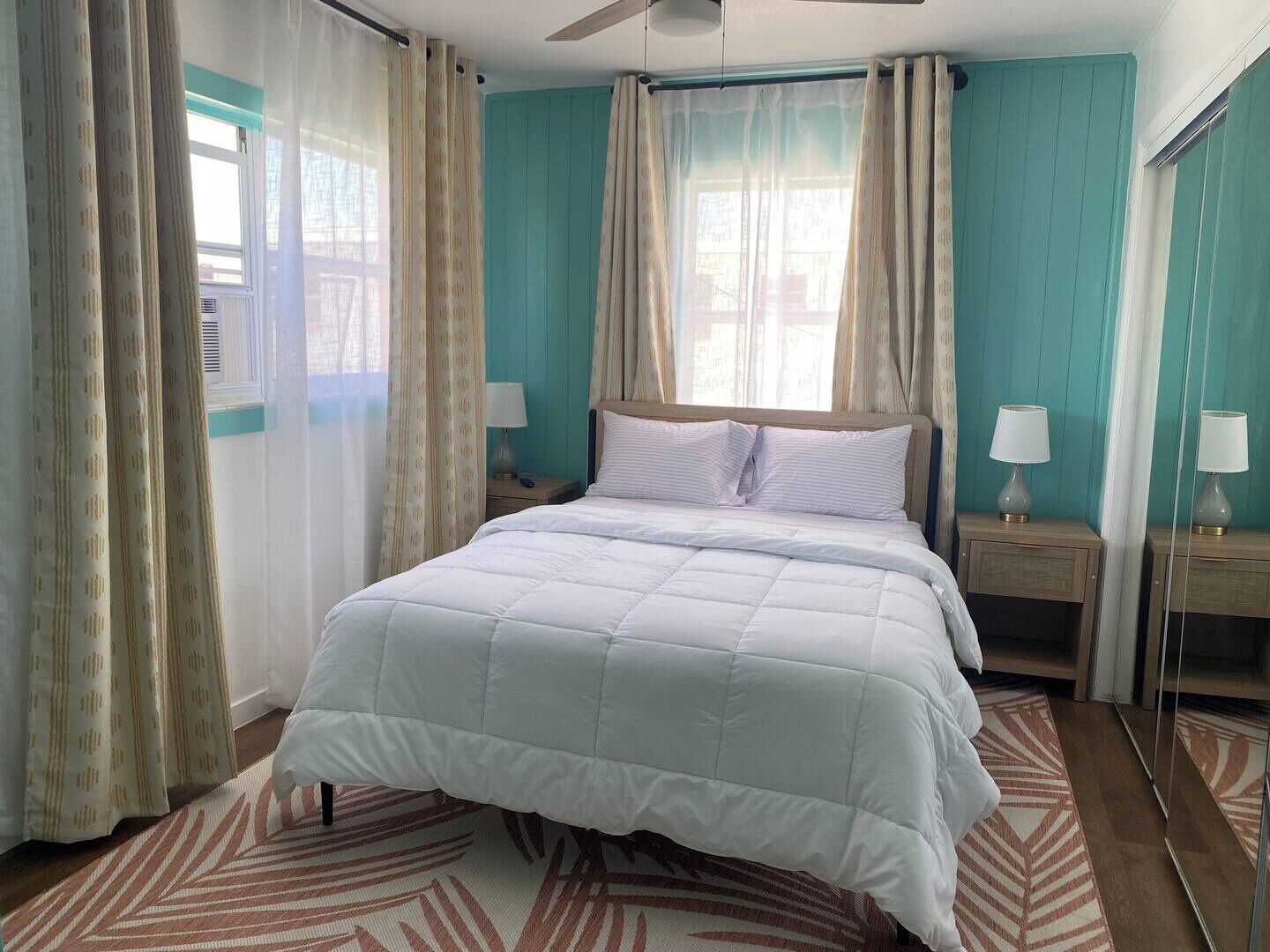 Un dormitorio con una cama, dos mesitas de noche con lámparas, una ventana con cortinas y un ventilador de techo.