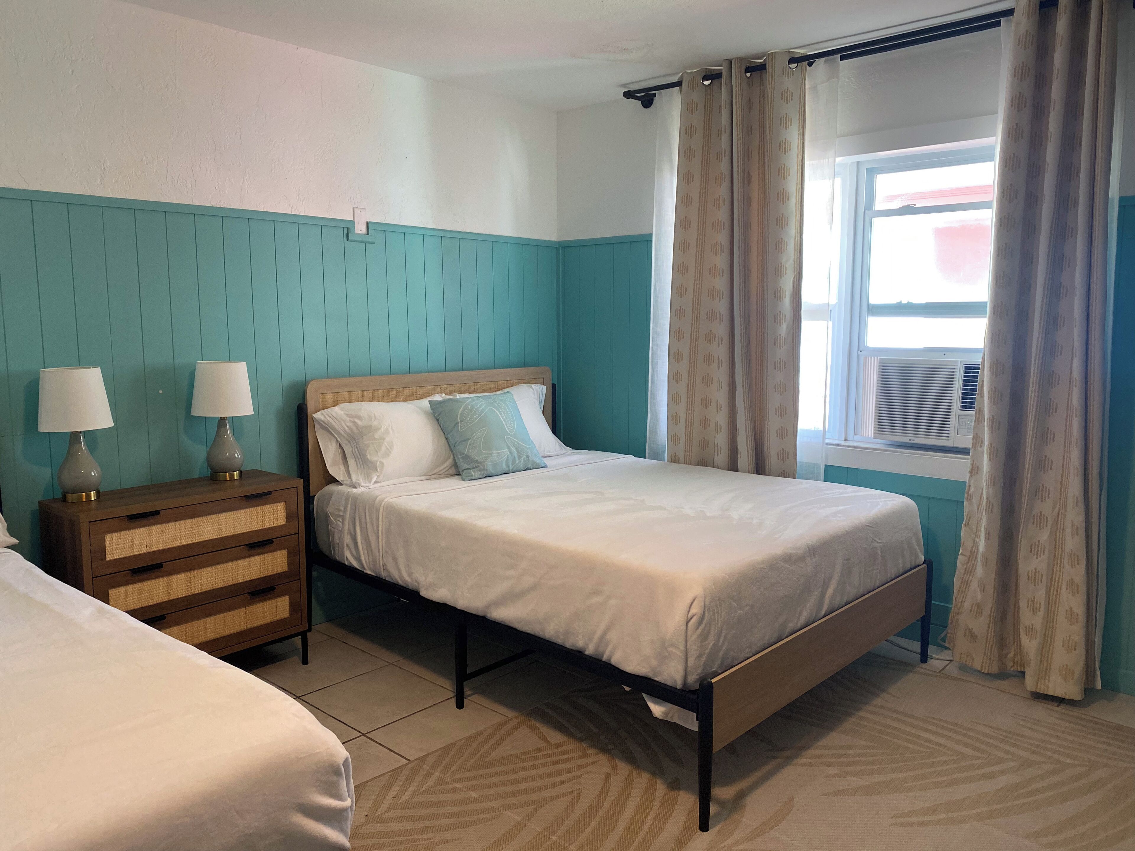 Un dormitorio con cama, mesitas de noche y una ventana con cortinas.