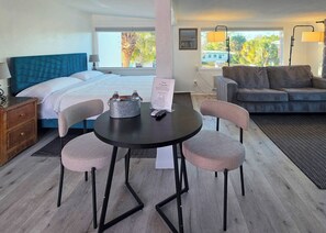 A hotel room with a bed, a dining table with chairs, a sofa, and a view of the outdoors. - Oasis Palms (Treasure Island)