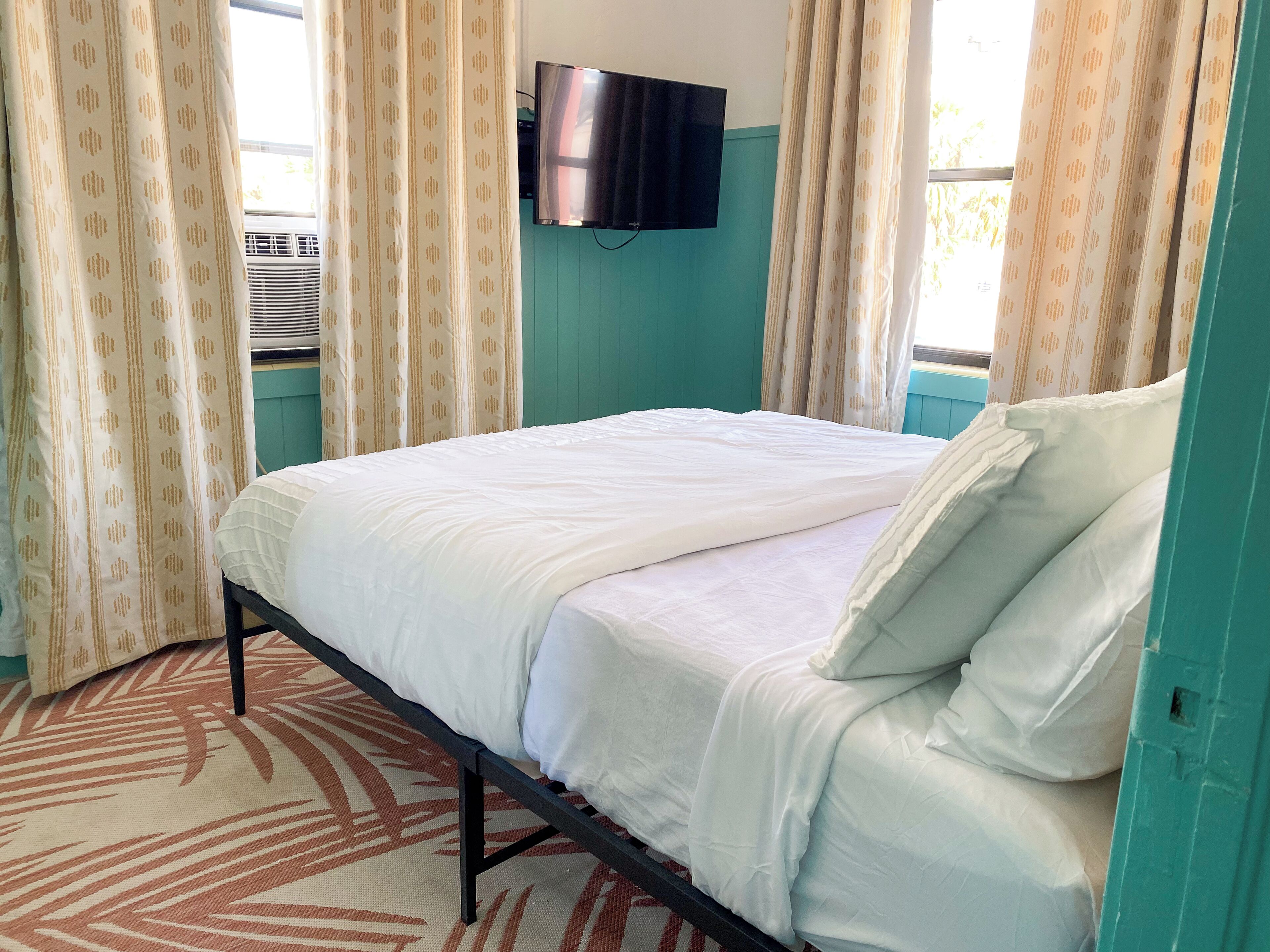 Quarto com cama, cortinas, televisão e janela.