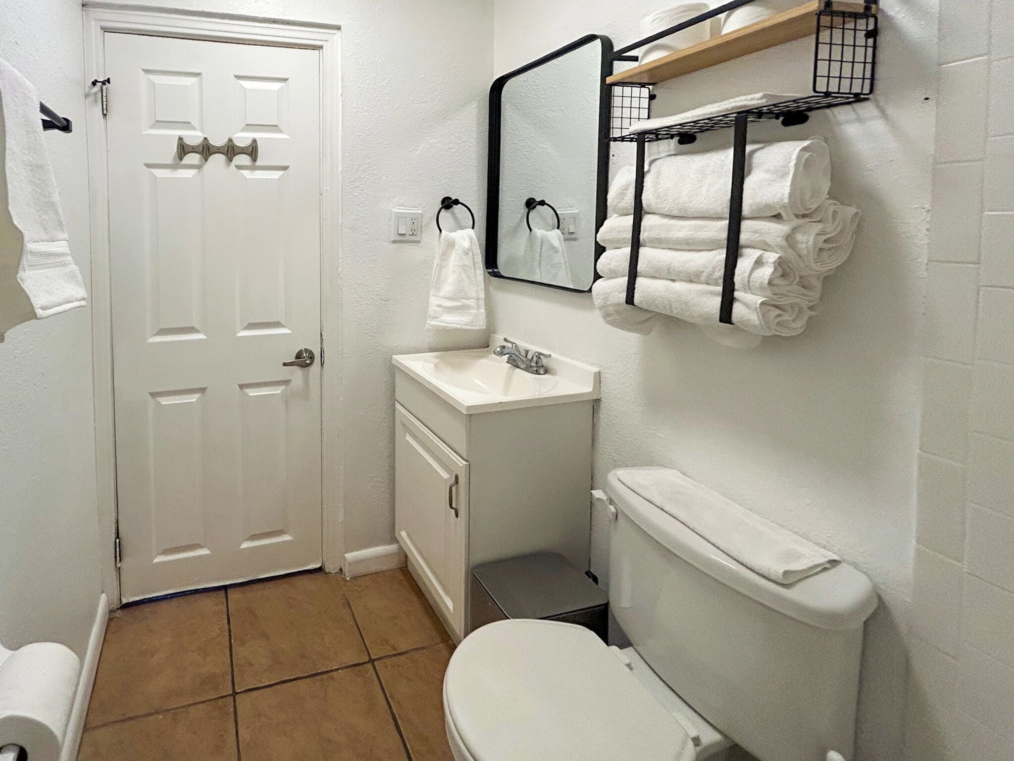 Un baño con puerta blanca, un lavabo, un inodoro y un perchero con toallas.