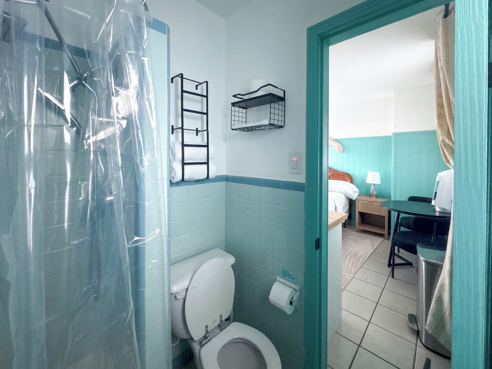A bathroom with a shower curtain, a toilet, a towel rack, and a small table with a lamp.