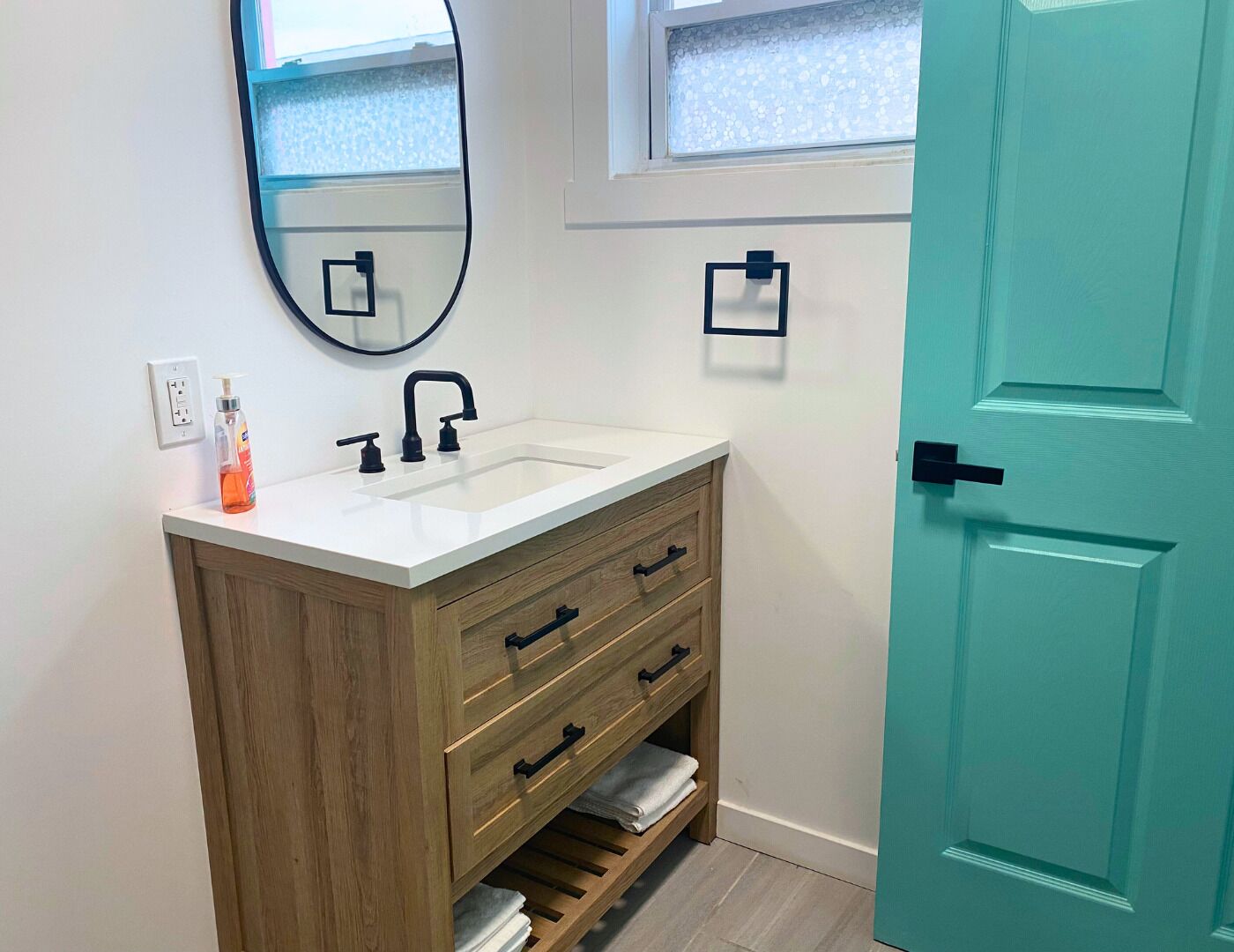 A bathroom with a white sink, wooden vanity, a mirror, and a teal door.