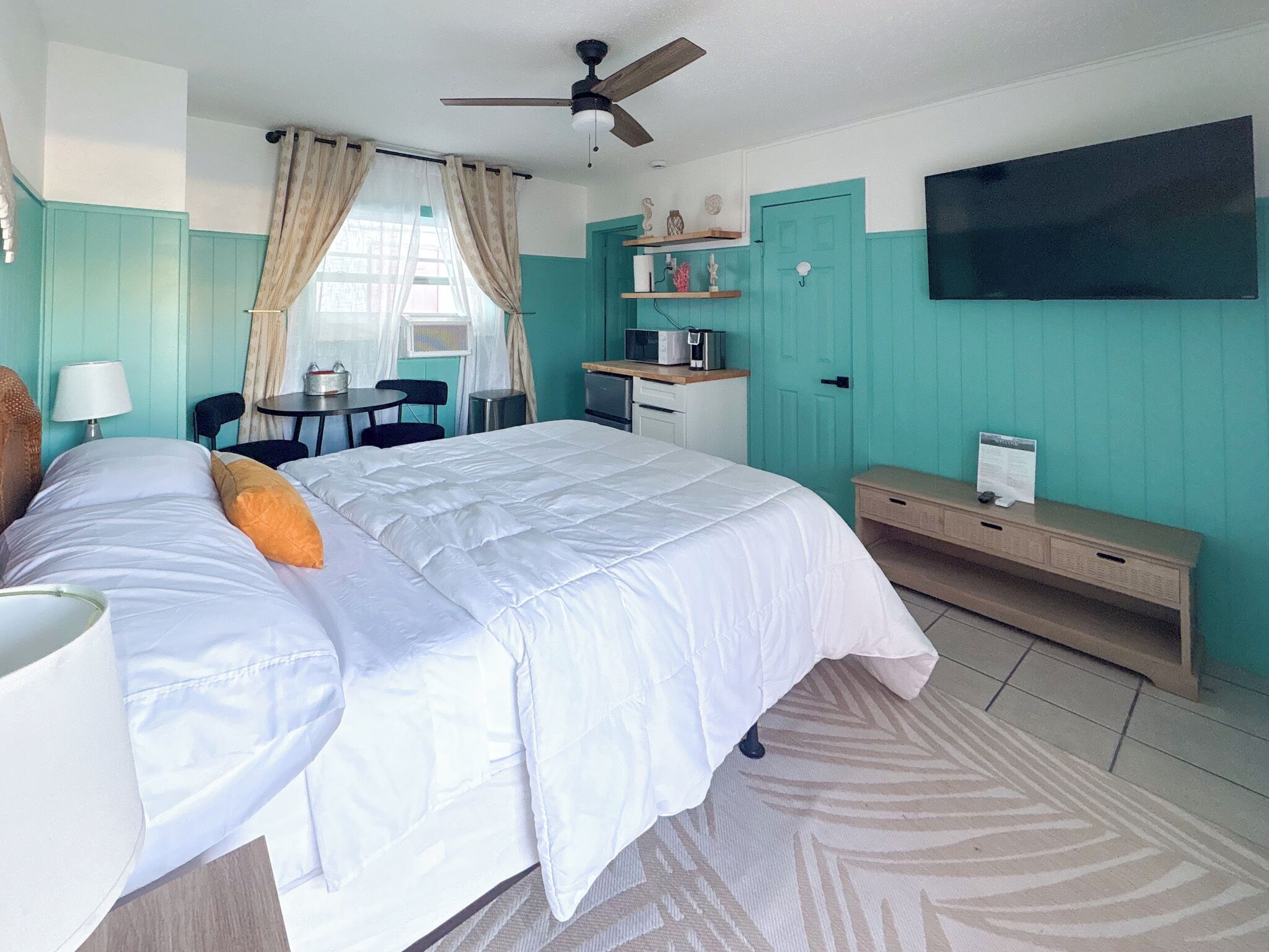 A bedroom with a bed, a desk, a chair, a television, and a ceiling fan.
