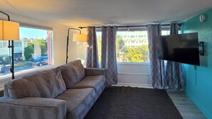 Een woonkamer met een bank, een vloerkleed, een televisie aan de muur en een raam met gordijnen.