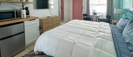 Un dormitorio con cama, escritorio, silla, televisor, microondas y cafetera.