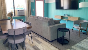 Een moderne woonkamer met een bank, een eettafel, stoelen, een televisie en een raam met gordijnen.