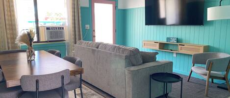 A modern living room with a sofa, dining table, chairs, a TV, and a window with curtains.