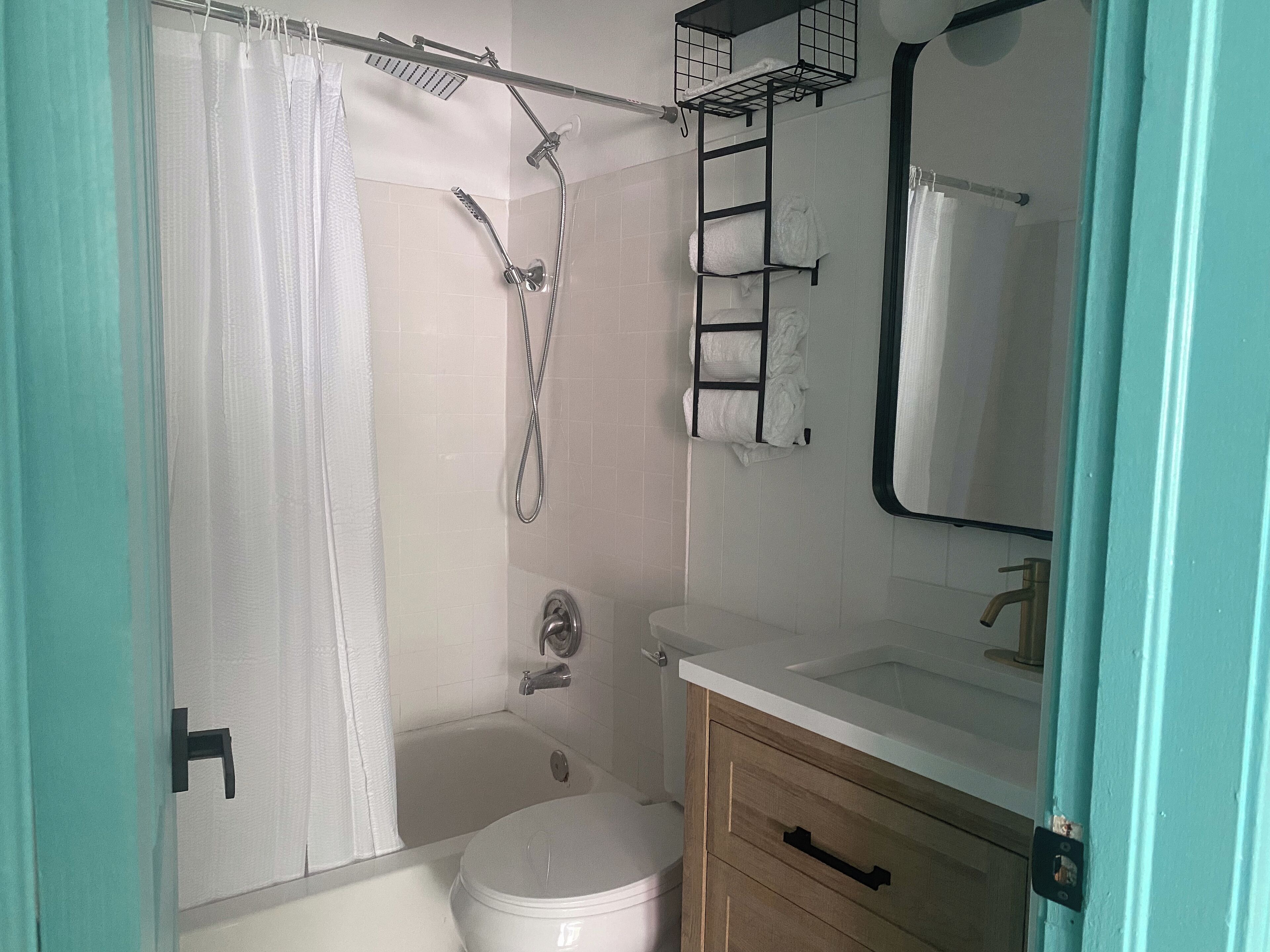 A bathroom with a shower, toilet, sink, and a mirror.