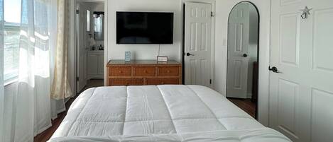 Un dormitorio con una cama grande, un televisor en la pared, un aparador de madera y puertas blancas.