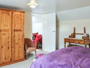 Een slaapkamer met een houten kast, een stoel, een bureau en een bed met een paarse deken.