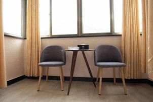 Una habitación con una pequeña mesa, dos sillas, una ventana con cortinas y suelo de madera.