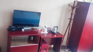 A compact room with a TV on a wooden desk, a small stool, and a wardrobe. - Taohuanyuan Hotel (Zongyang)