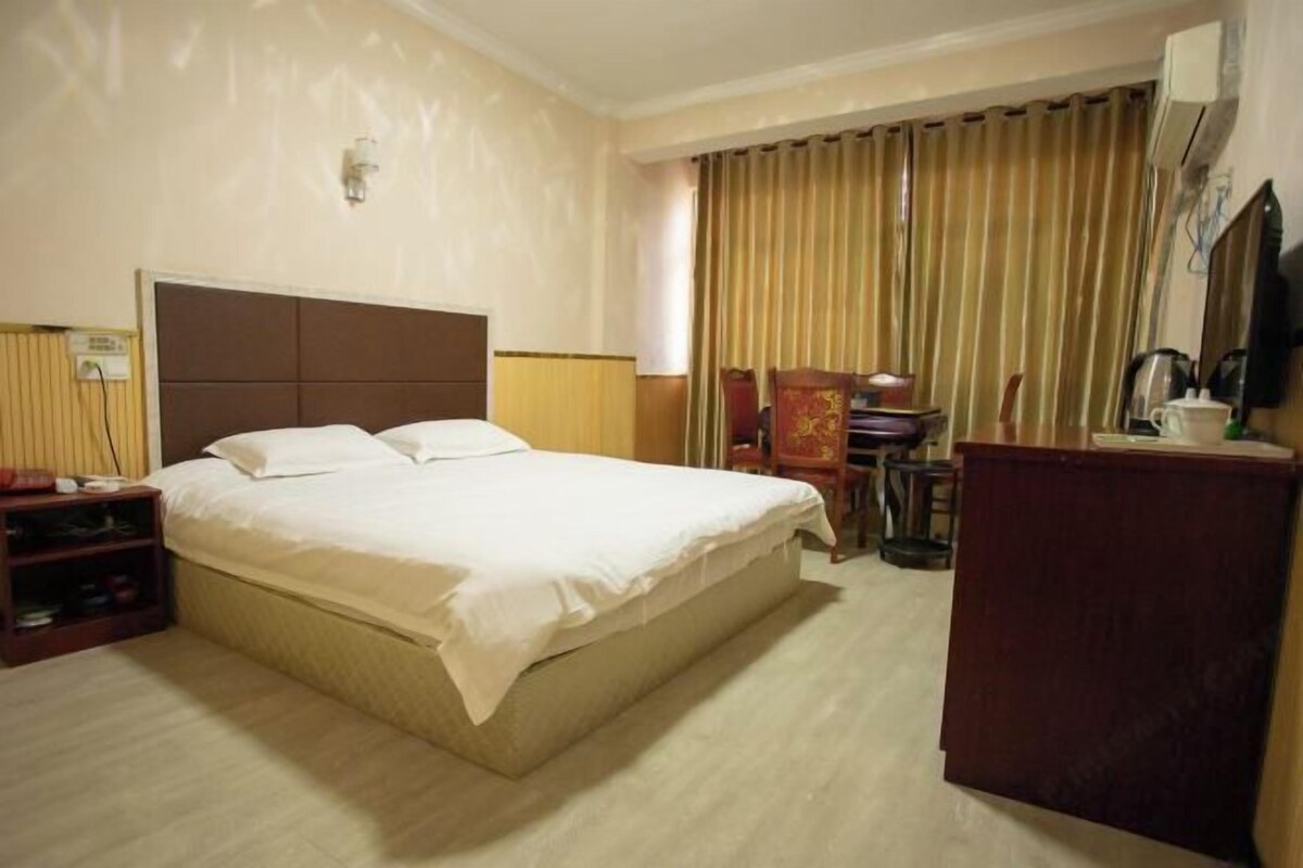 Ein Hotelzimmer mit Bett, Schreibtisch, Stuhl, Kleiderschrank und Vorhang.