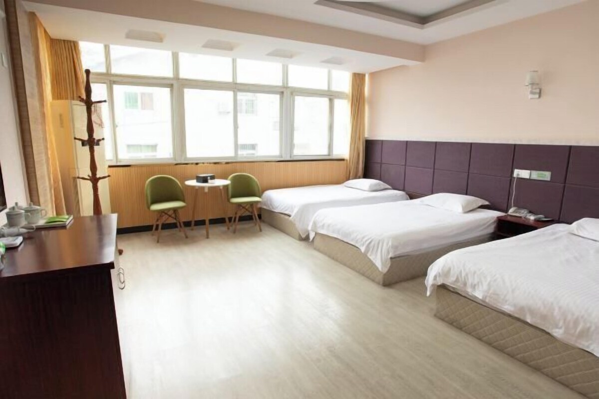 Ein Hotelzimmer mit zwei Betten, einem Schreibtisch mit Stuhl, einem Fenster mit Vorhängen und einem Nachttisch mit Lampe.