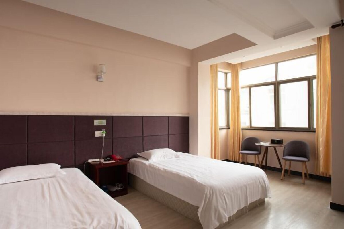 Ein Hotelzimmer mit zwei Betten, einem kleinen Tisch, zwei Stühlen, einem Nachttisch und einem Fenster mit Vorhängen.