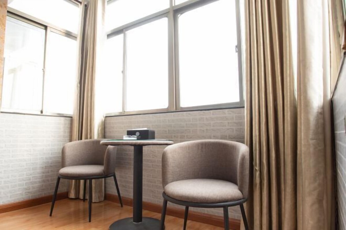 Ein Eckzimmer mit zwei Sesseln, einem kleinen Tisch und einem Fenster mit Vorhängen.