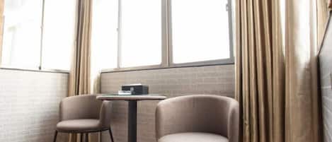 A corner room with two chairs, a small table, and a window with curtains.