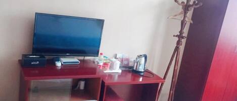 Una habitación con televisión, un escritorio con computadora, un hervidor y un armario.