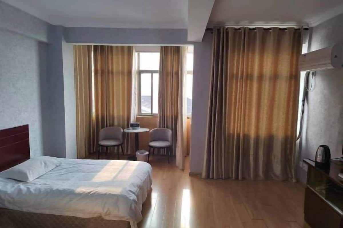 Et hotelværelse med seng, et lille bord med stole, et vindue med gardiner og et køleskab.