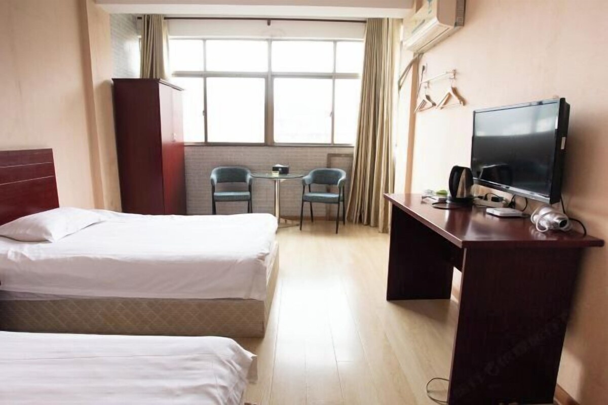 Ein Hotelzimmer mit zwei Betten, einem Schreibtisch mit Fernseher, einem kleinen Tisch und Stühlen.