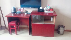 A red desk with a television, a chair, a trash can, and various items on the desk. - Taohuanyuan Hotel (Zongyang)