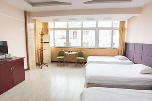 Habitación de hotel con dos camas, un escritorio con sillas, un televisor y una ventana con cortinas.
